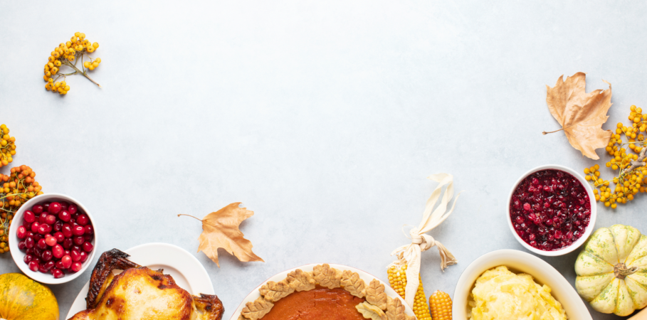 A festive Thanksgiving-themed flat lay featuring a roasted turkey, pumpkin pie decorated with pastry leaves, mashed potatoes, cranberry sauce, fresh cranberries, and small pumpkins. Seasonal decorations, including dried leaves, yellow berries, and corn, frame the scene on a light blue textured background, leaving ample space in the center.