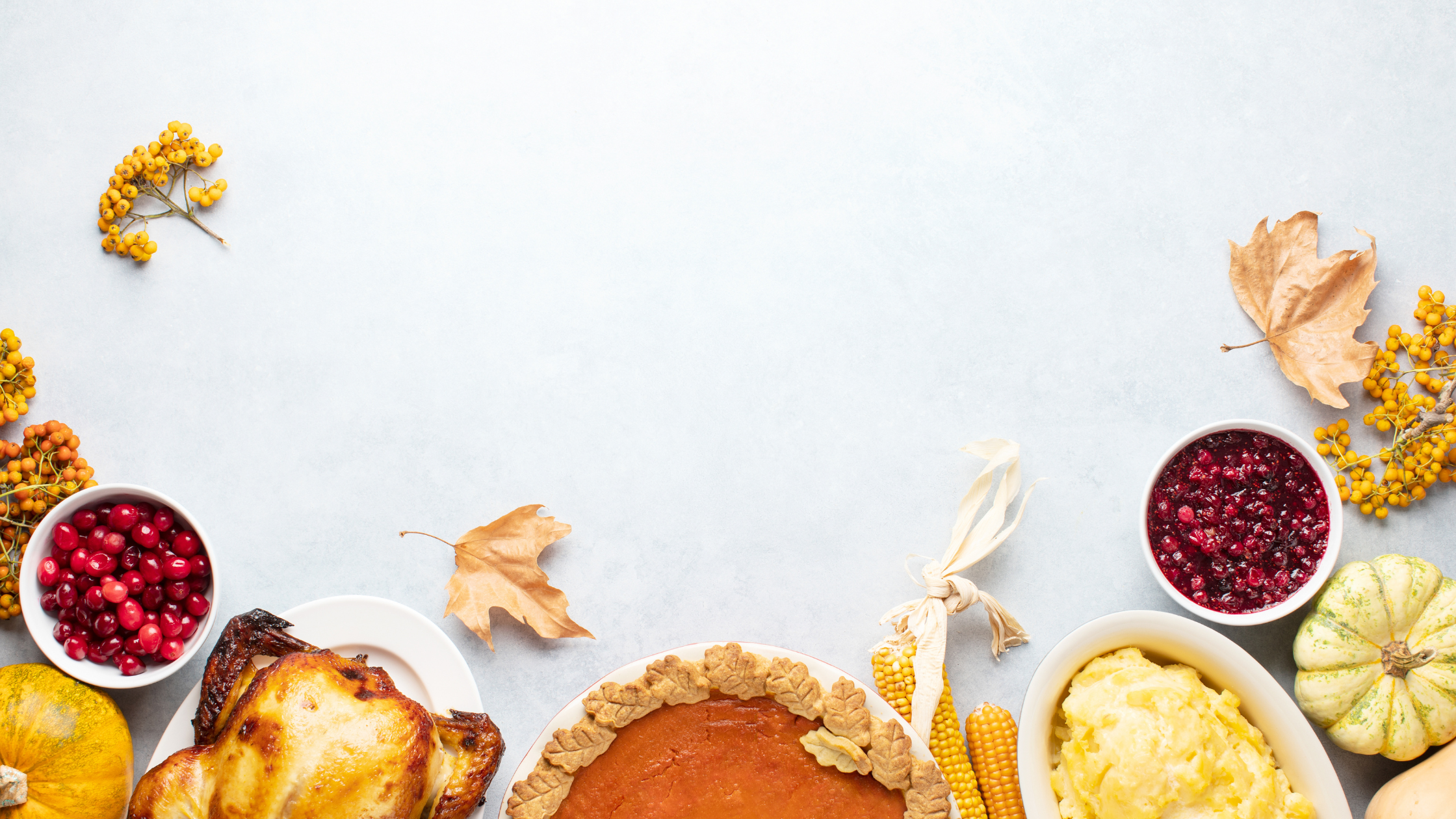 A festive Thanksgiving-themed flat lay featuring a roasted turkey, pumpkin pie decorated with pastry leaves, mashed potatoes, cranberry sauce, fresh cranberries, and small pumpkins. Seasonal decorations, including dried leaves, yellow berries, and corn, frame the scene on a light blue textured background, leaving ample space in the center.